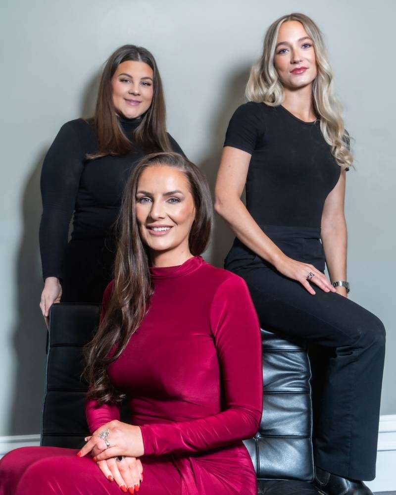 Three women smile at the camera, staff of the company